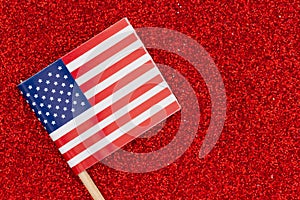 Closeup of a small American paper flag on red glitter textured paper