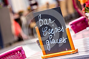 Small black board menu indicating bar, ice-creams and pancakes (Bar Crepes Glaces in French) on a table outside photo