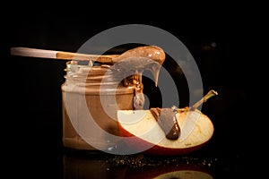 closeup small glass jar with peanut butter next to sliced apple