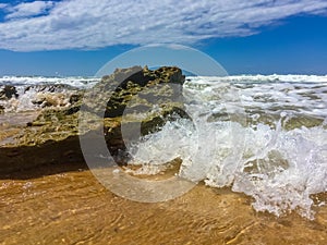 A closeup of a small wave hitting a rock on the beach