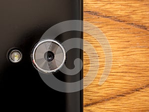 Closeup of a smart phone camera with lighting flash. On the right side of the photo empty background with wooden background