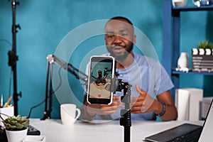 Closeup of smartphone filming influencer sitting down at desk with laptop smiling