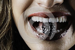 Closeup of a smiling blonde woman with production makeup and artistic effects biting into a wet cranberry