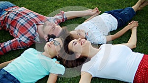 Family lying in circle on grass outdoors. Parents and children holding hands