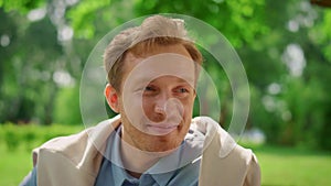 Closeup smiling man on nature. Portrait of handsome blond guy sitting on meadow.