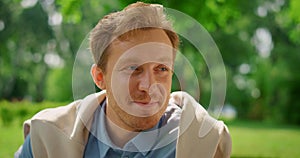 Closeup smiling man on nature. Portrait of handsome blond guy sitting on meadow.