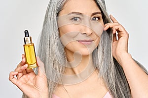 Closeup of smiling mid age Asian woman holding hair and skin care oil serum.