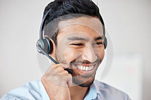 Closeup of smiling mixed race call centre agent smiling while wearing headset. Young male customer service