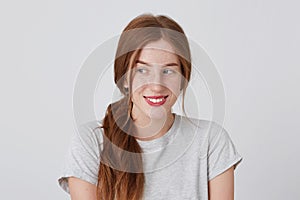 Closeup of smiling pretty redhead young woman with freckles wears gray t shirt feels happy and looks to the side isolated over