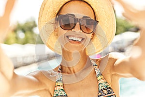 Closeup smiling woman in hat and sunglasses making selfie against summer background.