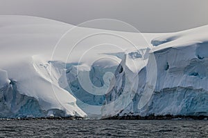 Closeup, snow and blue ice, Antarctic Peninsula. Small inlet in center. Clouds in background. Calm sea in foreground.