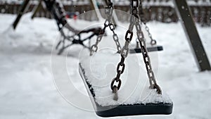 Closeup of snow slowly covering empty chain swings on winter children playground at park