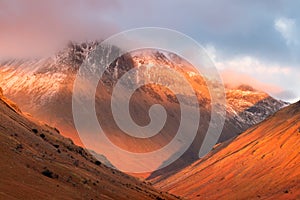 Closeup snowcapped mountain range covered in thick cloud with vibrant red sunlight colours. Great Gable, Lake District, UK.