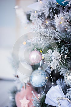 Closeup snowy tree branch with pastel Christmas balls on blurred bokeh background