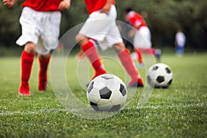 Closeup of soccer ball on grass pitch. Kid kicking classic black and white football balls on training