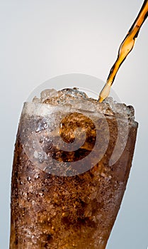 Closeup of soft drink pouring to glass with crushed ice cubes is