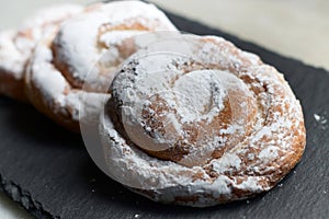 closeup of some ensaimadas with icing sugar on a slate table