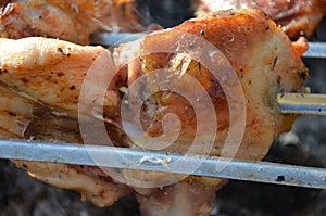 Closeup of some meat skewers being grilled in a barbecue. pieces of chicken leg meat roasting on the corners of skewers
