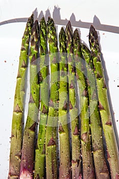 closeup of some raw green asparagus on a white plate, white background top view