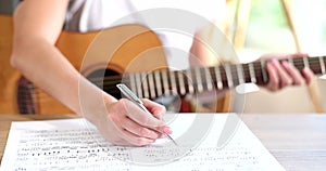 Closeup songwriter enjoys hobby with pleasure and writes musical notes on paper with acoustic guitar