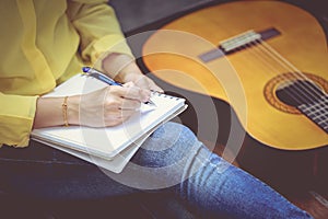 Closeup songwriter writing on note paper with acoustic guitar ne