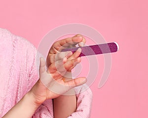 Closeup. Sophisticated young lady teen girl in bathrobe makes manicure with nail file on pink