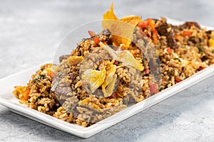 Closeup of spicy cooked rice with meat, vegetables and chips in a plate on the table