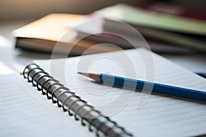 Spiral bound notebook with blue pencil, blurred background suggests books or folders photo