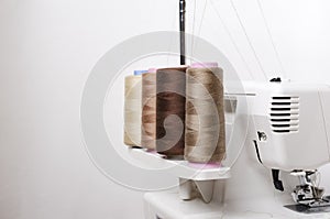 Closeup of spool of beige threads and professional overlock macnine against white background photo