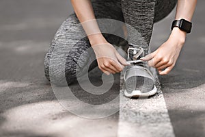 Closeup Of Sporty Female Tying Shoes Before Running Outdoors, Cropped Image