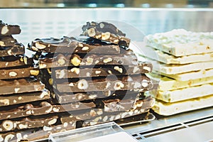Closeup stack of assortment luxury handmade chocolate, dark and white chocolate bars with nuts in shop window.