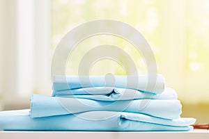 Closeup stack of blue clean bedding on blurred background. Sunlight from the window