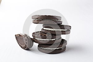 Stack of dark sandwich cookies and piece of it on the white background photo