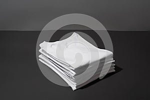 Closeup of a stack of folded white cotton t shirts isolated over dark gray background