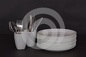 Closeup of stacked plates on the table with knives and forks in mugs isolated on a black background