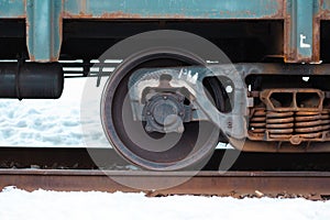 A closeup of a steel wheel of a train on the rail during a snowy winter. Rusty springs on the right side of the frame