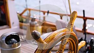 Closeup of a steering wheel and deck of a wooden antique Sail boat navigating in the ocean sunny day showing the wooden parts and
