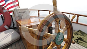 Closeup of a steering wheel and deck of a wooden antique sail boat navigating in the ocean sunny day showing the wooden parts and