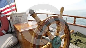 Closeup of a steering wheel and deck of a wooden antique sail boat navigating in the ocean sunny day showing the wooden parts and