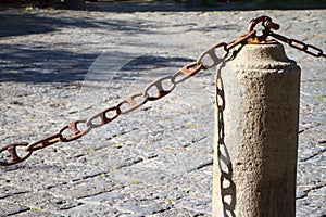 Closeup of a stone fence pillar and chain on a stone pavement background