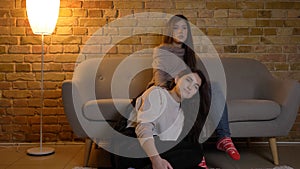 Closeup straight portrait of two young pretty women watching a movie TV sitting laidback on the floor in a cozy