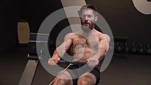 Closeup straight shoot of adult motivated athletic shirtless man using rowing machine and making resistance training