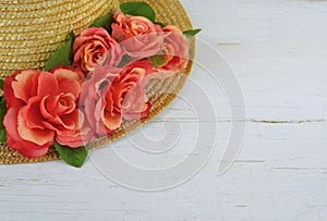 Closeup of a straw bonnet decorated with multiple silk roses on a white washed wooden background with copy space. Good for spring