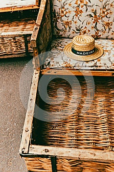 Closeup of a straw hat with 'Maderia' written on it resting on a floral chair. Maderia Funchal