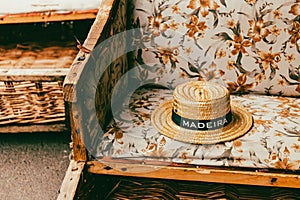 Closeup of a straw hat with 'Maderia' written on it resting on a floral chair. Maderia Funchal