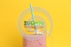 Closeup of a strawberry smoothie inside an aesthetically cute mason jar mug with green cap and straw