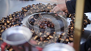 Closeup street seller roasting chestnuts in hot pan in outdoor cafe. Roasted chestnut selling on food street. Local