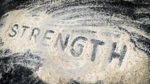 Closeup of STRENGTH text written on white sand