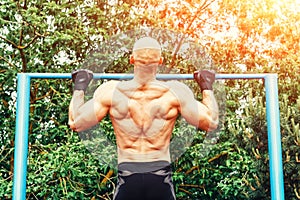 Closeup of strong bald athlete doing pull-up on horizontal bar. back view.