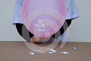 Closeup student do science experiment about static electricty from pink balloon and pieces of paper.